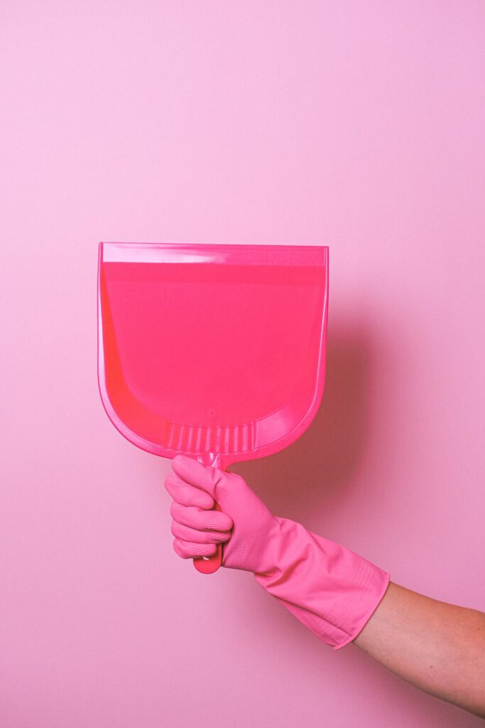Hand in rubber glove holds a pink dustpan