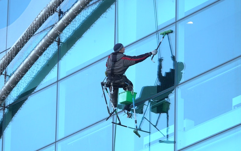 Man from a hired cleaning crew cleaning windows of commercial offices.