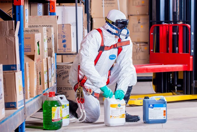 Man in suit and mask holding cleaning chemicals