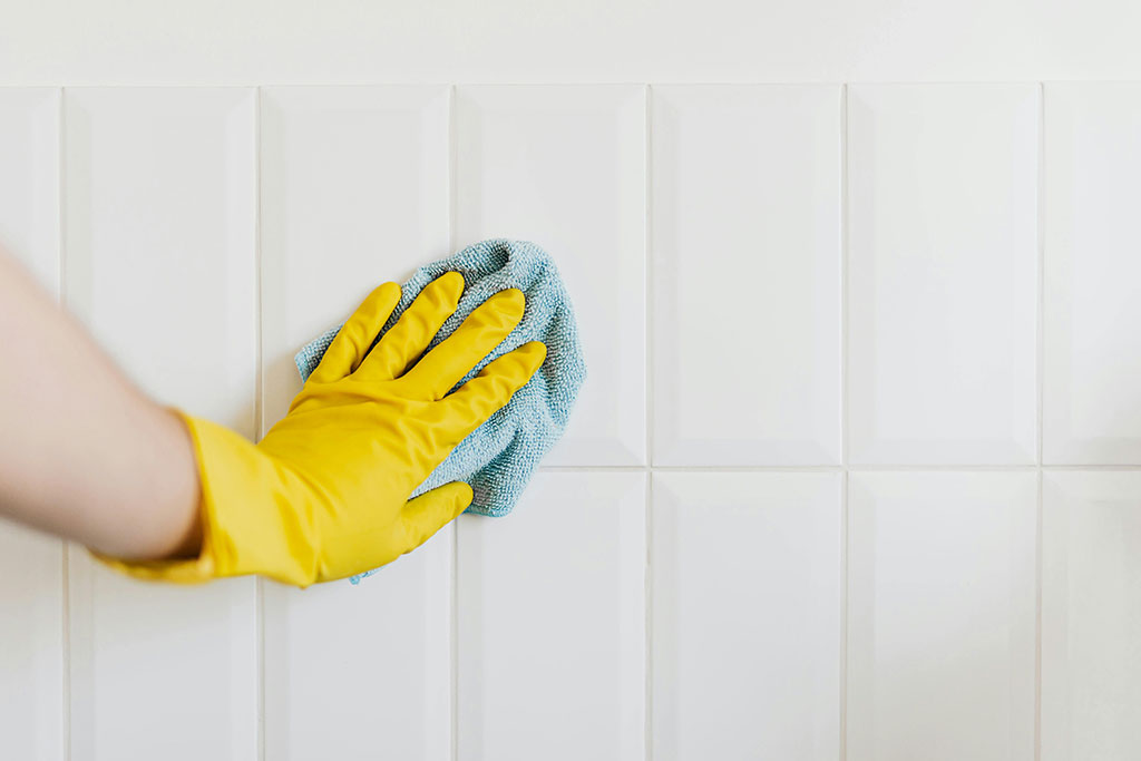 Gloved hand cleaning bathroom tiles